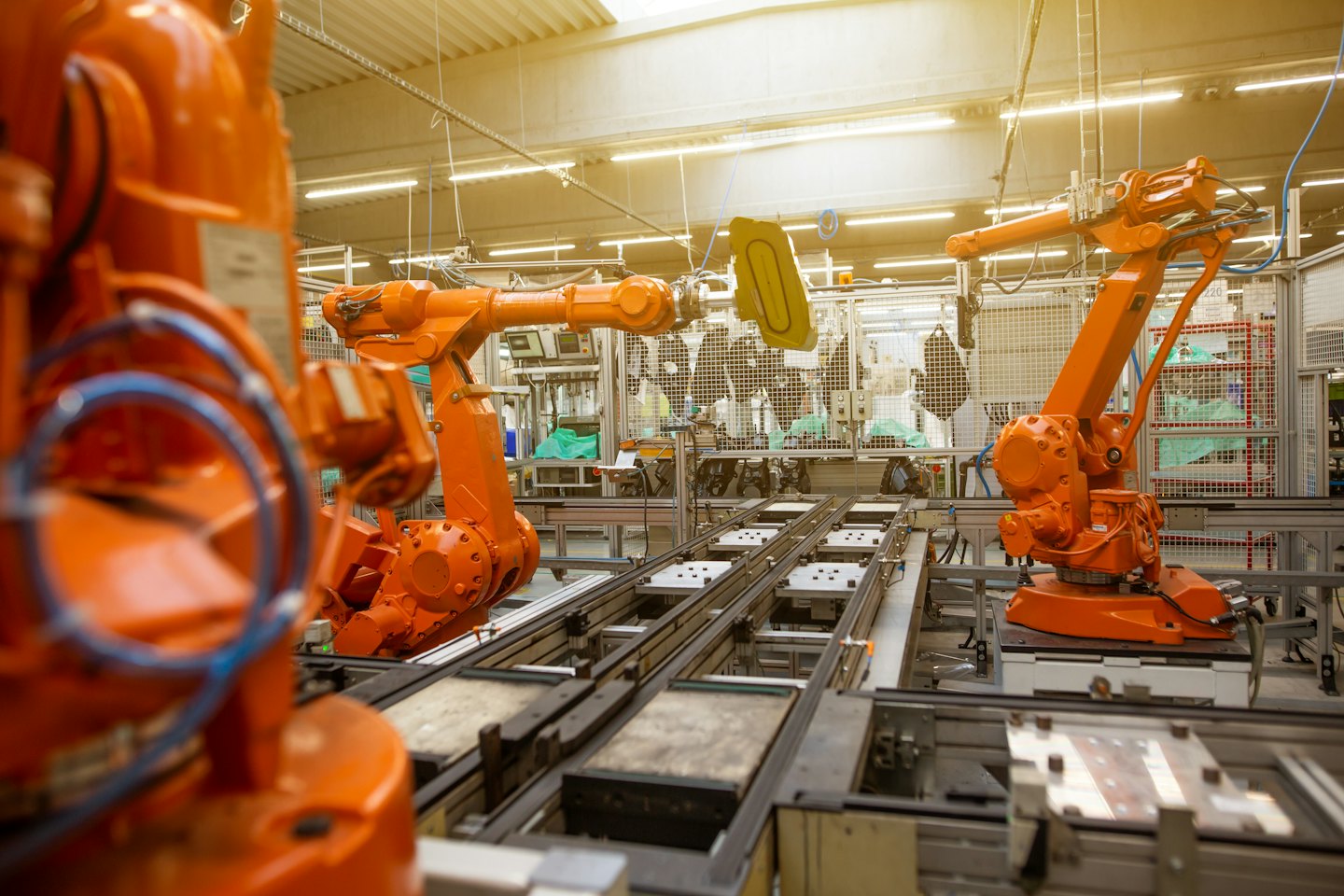 Robotic arms assemble components on a brightly lit factory floor.